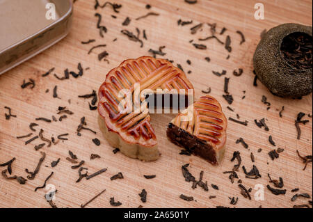 Preparation to the Chinese Mid-Autumn festival concept. Traditional food for the holiday delicious Moon cake on the wooden tray with black pu`er tea. Stock Photo